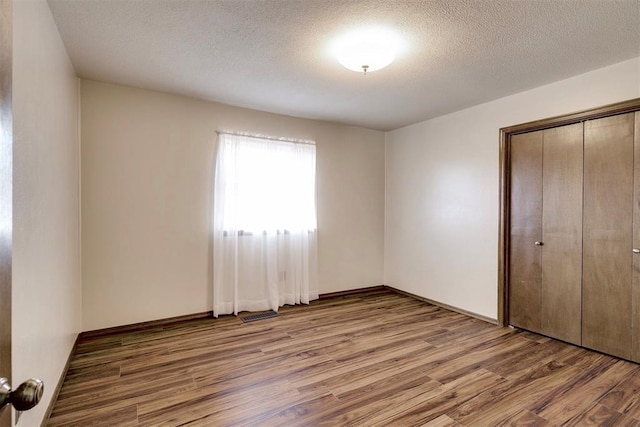 unfurnished bedroom featuring a closet, visible vents, a textured ceiling, and wood finished floors