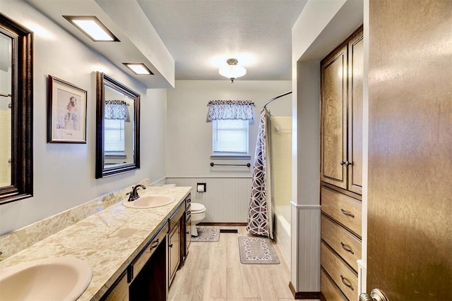 full bathroom featuring a wainscoted wall, toilet, a sink, a textured ceiling, and wood finished floors