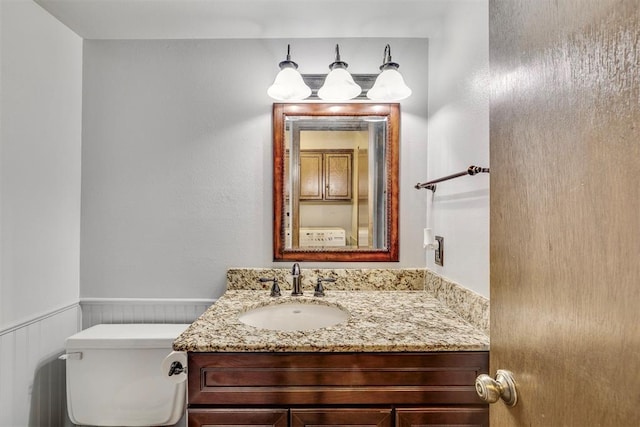 half bath featuring a wainscoted wall, toilet, and vanity