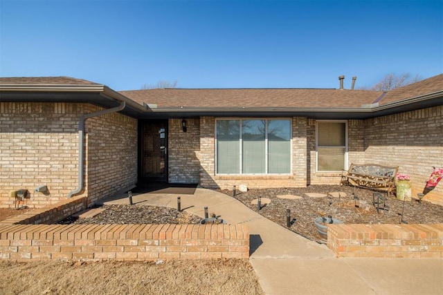 view of exterior entry with brick siding and a shingled roof