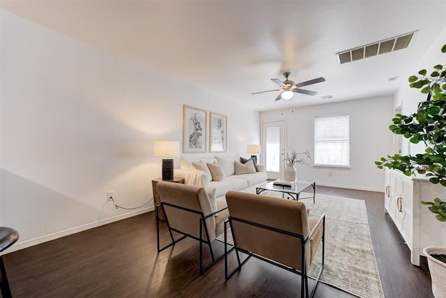 living room featuring visible vents, ceiling fan, baseboards, and dark wood-style flooring