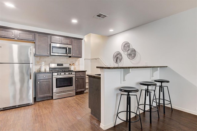 kitchen with dark wood-style floors, visible vents, stainless steel appliances, a kitchen breakfast bar, and tasteful backsplash