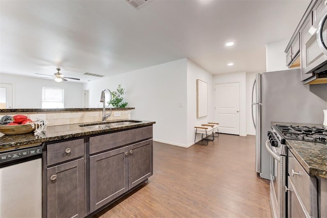 kitchen featuring dark brown cabinets, dark stone counters, dark wood-style floors, stainless steel appliances, and a sink