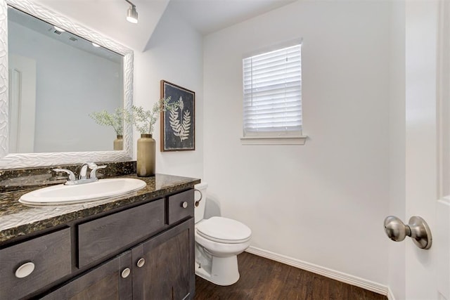 half bathroom with vanity, toilet, wood finished floors, and baseboards