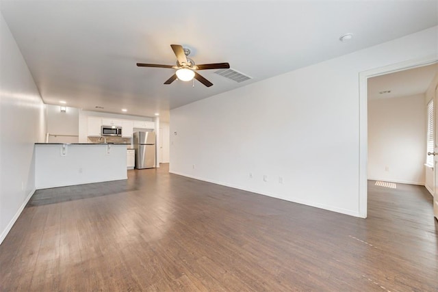 unfurnished living room with baseboards, visible vents, dark wood-style flooring, and ceiling fan