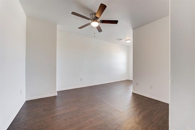 spare room featuring ceiling fan, visible vents, baseboards, and dark wood finished floors