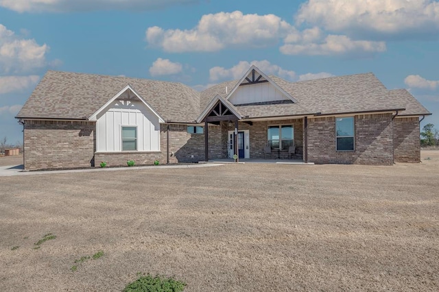 view of front of house with board and batten siding, brick siding, and roof with shingles