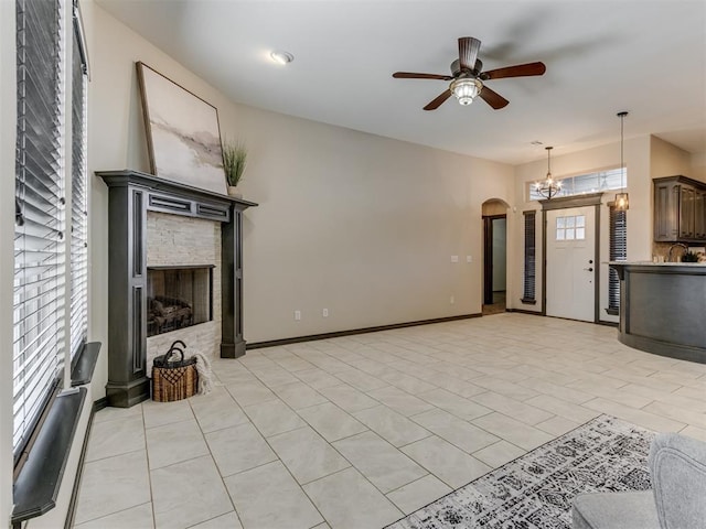 living room featuring ceiling fan with notable chandelier, a fireplace, arched walkways, and baseboards