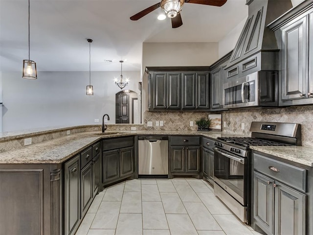 kitchen featuring tasteful backsplash, light stone countertops, appliances with stainless steel finishes, a peninsula, and a sink