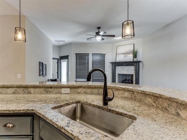 kitchen with light stone counters, visible vents, a fireplace, a sink, and open floor plan