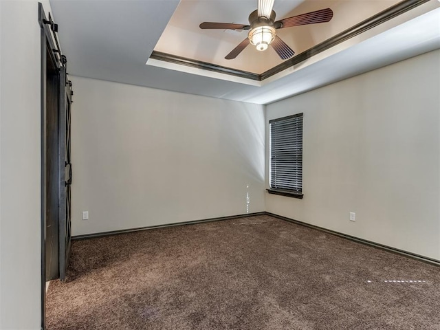 carpeted spare room with ceiling fan, baseboards, a raised ceiling, and a barn door