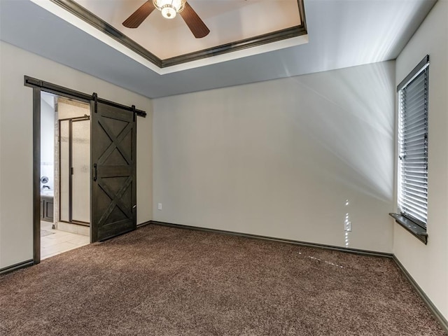 carpeted empty room featuring a tray ceiling, a barn door, baseboards, and plenty of natural light