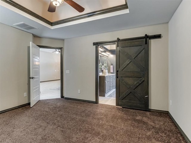 empty room featuring a ceiling fan, visible vents, carpet floors, a tray ceiling, and a barn door