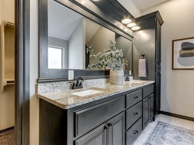 full bath featuring tile patterned flooring, double vanity, baseboards, and a sink