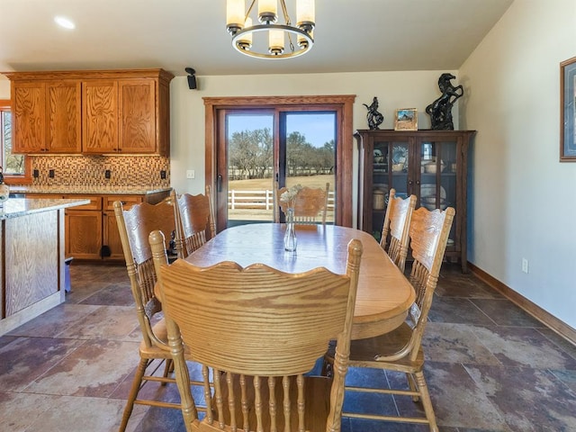 dining space featuring baseboards, a chandelier, and stone finish floor