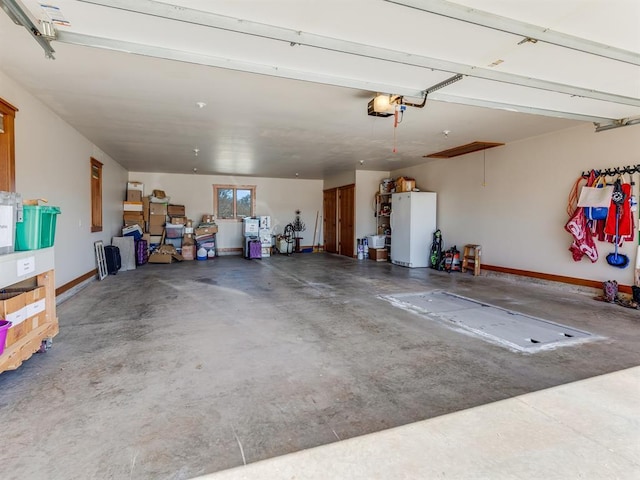 garage with a garage door opener, freestanding refrigerator, and baseboards