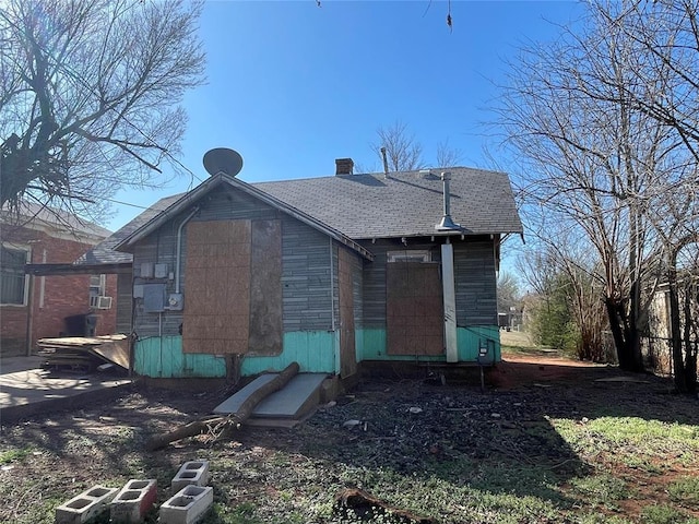 rear view of house featuring cooling unit, a chimney, and roof with shingles