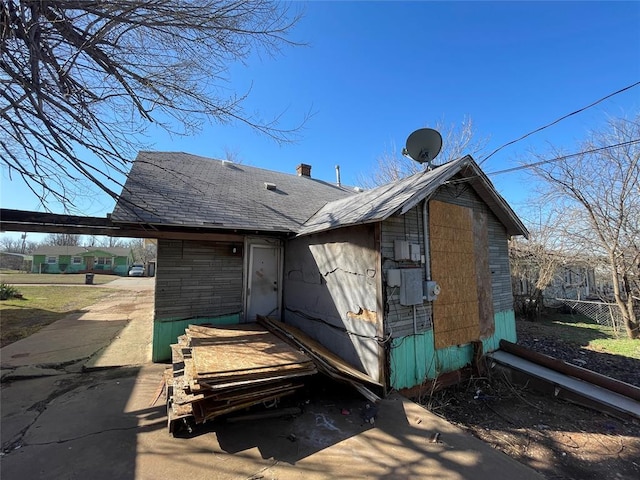 rear view of house with a chimney, roof with shingles, and fence