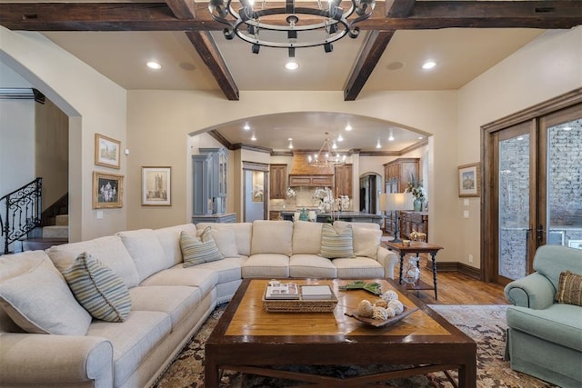 living room with stairs, beam ceiling, light wood-style flooring, arched walkways, and a notable chandelier