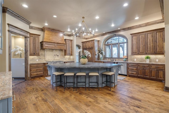 kitchen with custom exhaust hood, appliances with stainless steel finishes, a breakfast bar, and wood finished floors