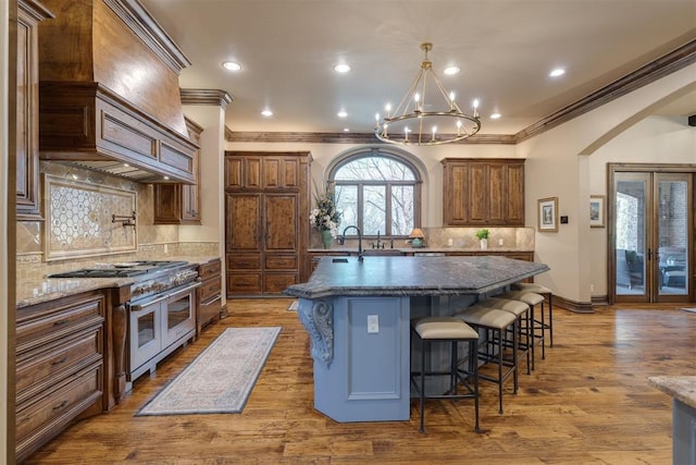 kitchen with a breakfast bar, range with two ovens, arched walkways, a kitchen island with sink, and dark wood-style flooring