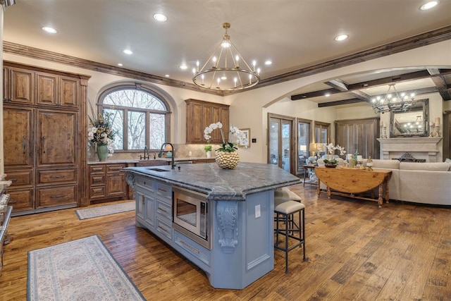 kitchen with stainless steel microwave, a notable chandelier, a breakfast bar area, and a kitchen island with sink