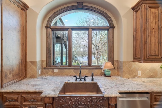 kitchen with backsplash, dishwasher, light stone countertops, and a sink