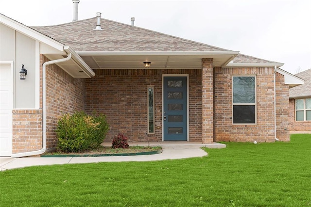 doorway to property with an attached garage, a lawn, brick siding, and a shingled roof