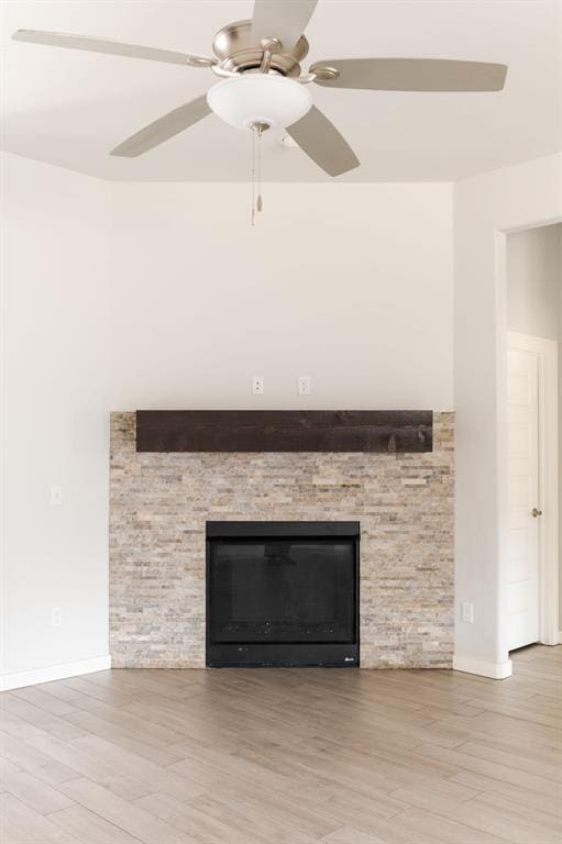 room details with baseboards, wood finished floors, a stone fireplace, and ceiling fan