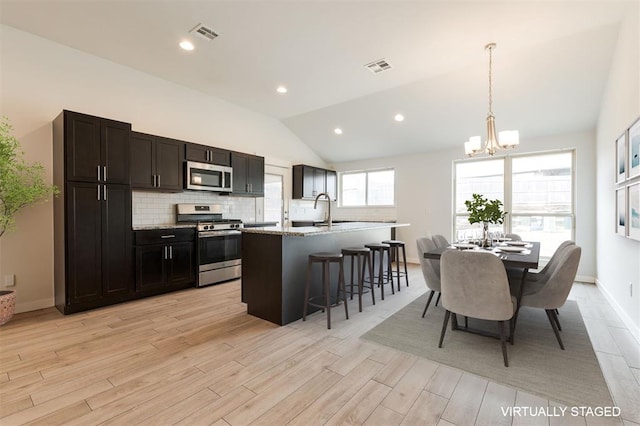 kitchen with visible vents, an inviting chandelier, stainless steel appliances, decorative backsplash, and vaulted ceiling