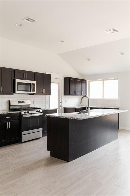 kitchen with light stone countertops, lofted ceiling, decorative backsplash, stainless steel appliances, and a sink