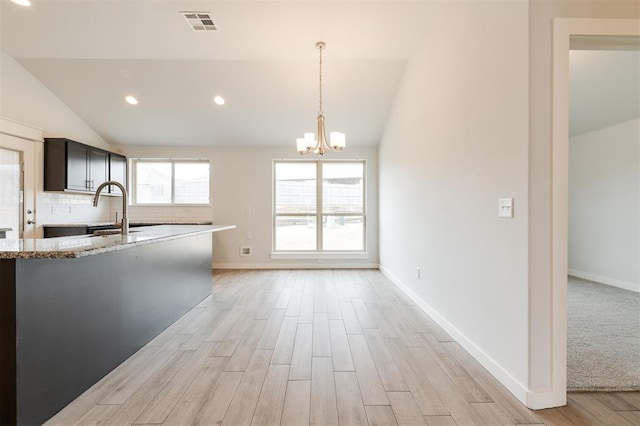 kitchen with light wood finished floors, backsplash, vaulted ceiling, an inviting chandelier, and a sink