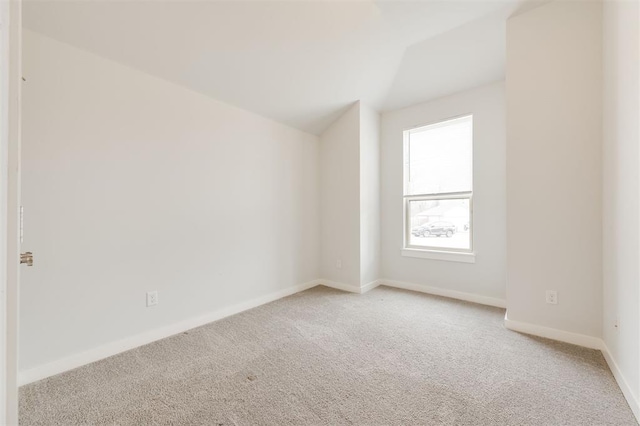 empty room with light carpet, baseboards, and vaulted ceiling