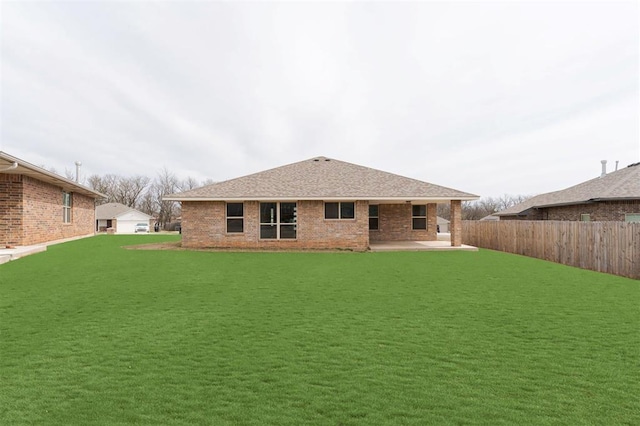 back of property with a patio, fence, a yard, a shingled roof, and brick siding