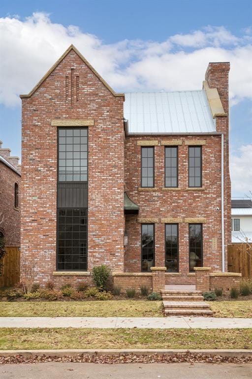 view of front of house featuring a standing seam roof, brick siding, a chimney, and metal roof