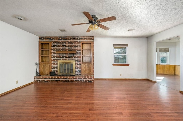 unfurnished living room with a wealth of natural light, built in shelves, a textured ceiling, and wood finished floors