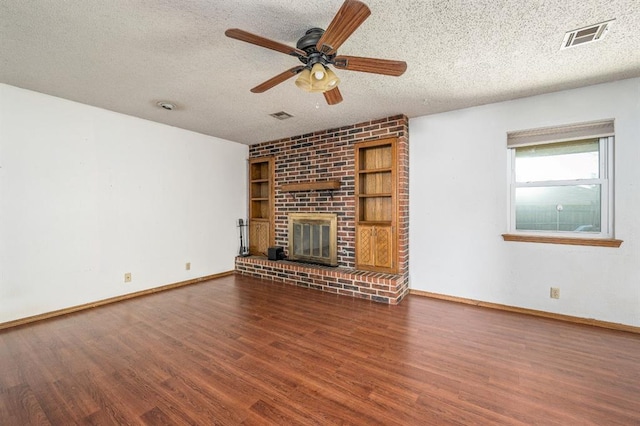 unfurnished living room featuring visible vents, a brick fireplace, a textured ceiling, and wood finished floors