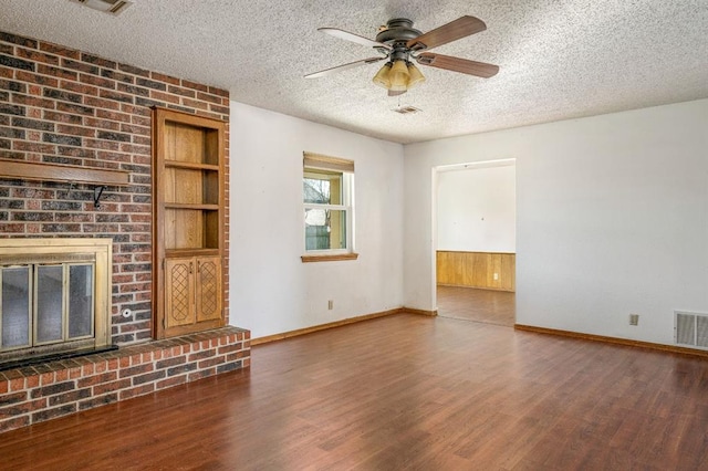 unfurnished living room with visible vents, built in shelves, a textured ceiling, wood finished floors, and a brick fireplace