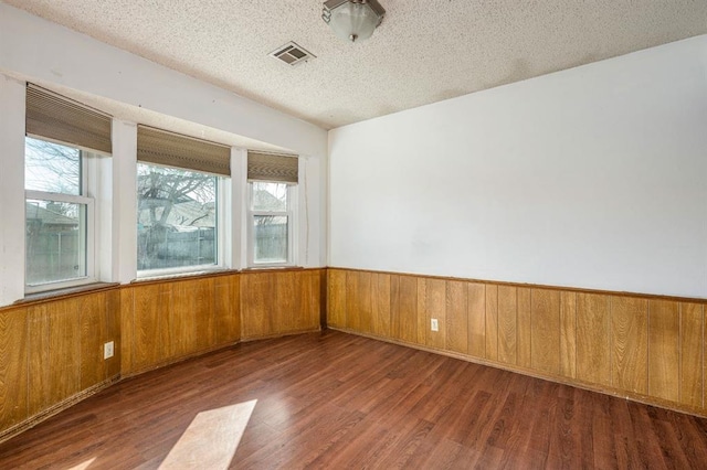 unfurnished room featuring visible vents, a wainscoted wall, wood walls, wood finished floors, and a textured ceiling