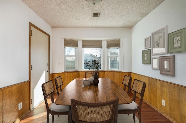 dining room with a wainscoted wall, visible vents, a textured ceiling, and wooden walls