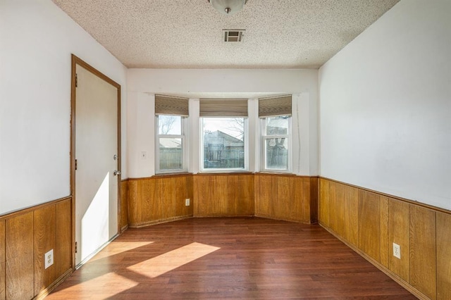 unfurnished room featuring visible vents, a wainscoted wall, wood walls, and a textured ceiling