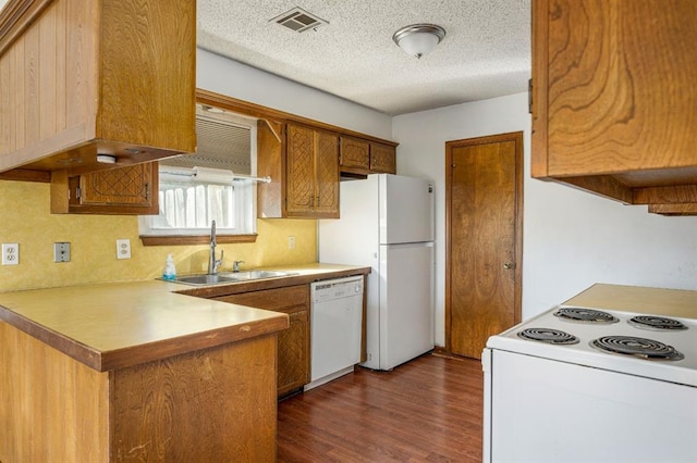 kitchen with visible vents, dark wood finished floors, a peninsula, white appliances, and a sink