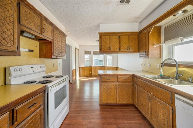 kitchen featuring white appliances, brown cabinetry, dark wood-style floors, visible vents, and a sink