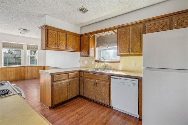 kitchen featuring visible vents, brown cabinets, wood finished floors, white appliances, and a sink