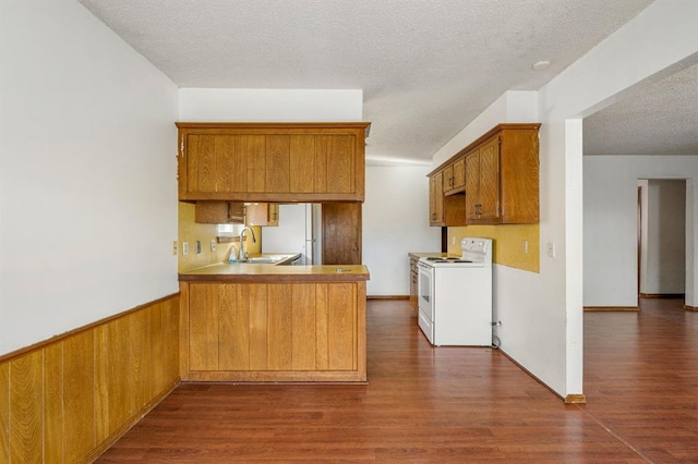 kitchen featuring white range with electric cooktop, a wainscoted wall, a peninsula, a textured ceiling, and dark wood-style flooring