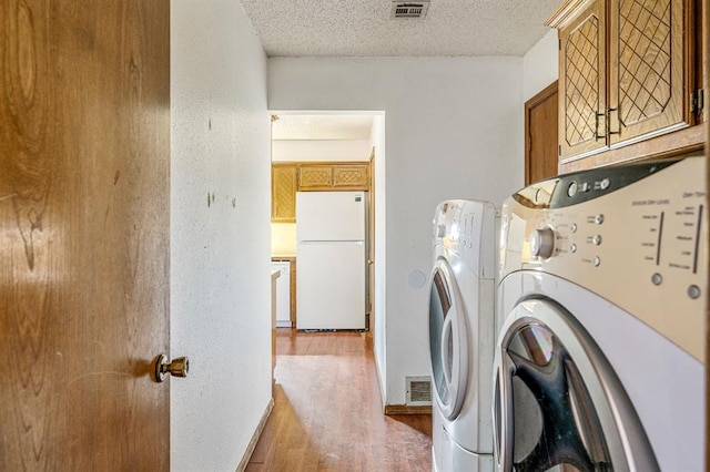 laundry room featuring visible vents, wood finished floors, cabinet space, a textured ceiling, and independent washer and dryer