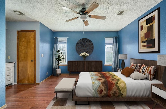 bedroom with visible vents, a textured ceiling, baseboards, and wood finished floors