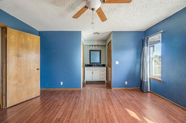 unfurnished living room featuring baseboards, a textured ceiling, wood finished floors, and a textured wall