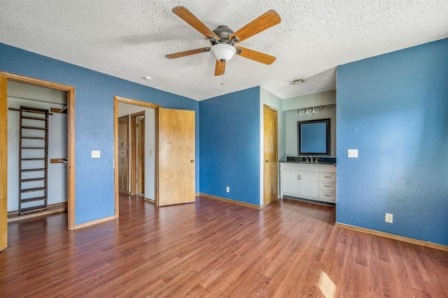 unfurnished bedroom featuring visible vents, a sink, baseboards, and wood finished floors