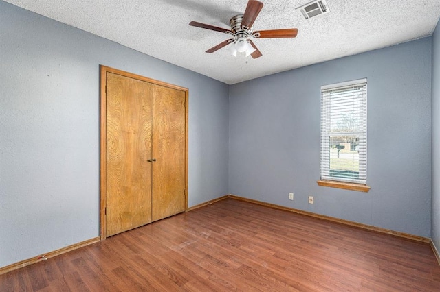 unfurnished bedroom featuring a textured ceiling, wood finished floors, visible vents, and baseboards